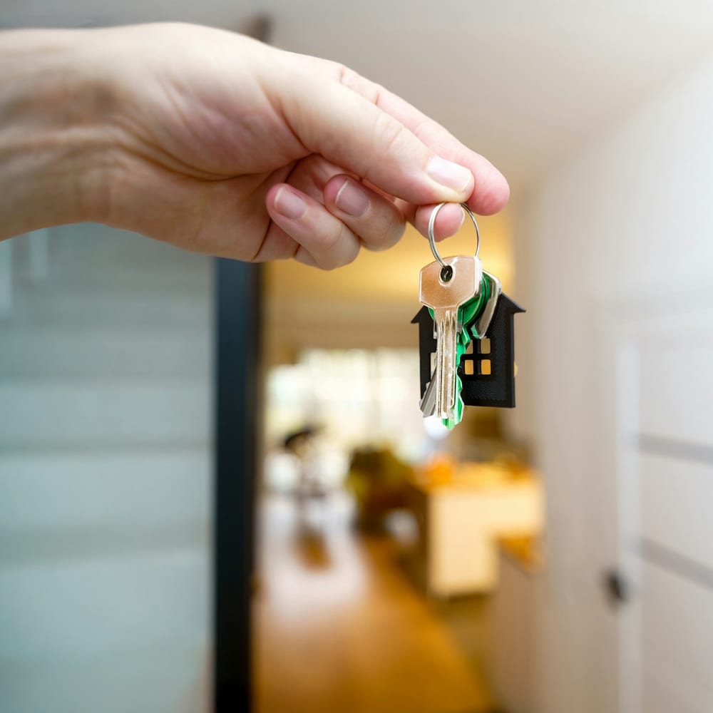 A hand holding house keys in a bright entryway